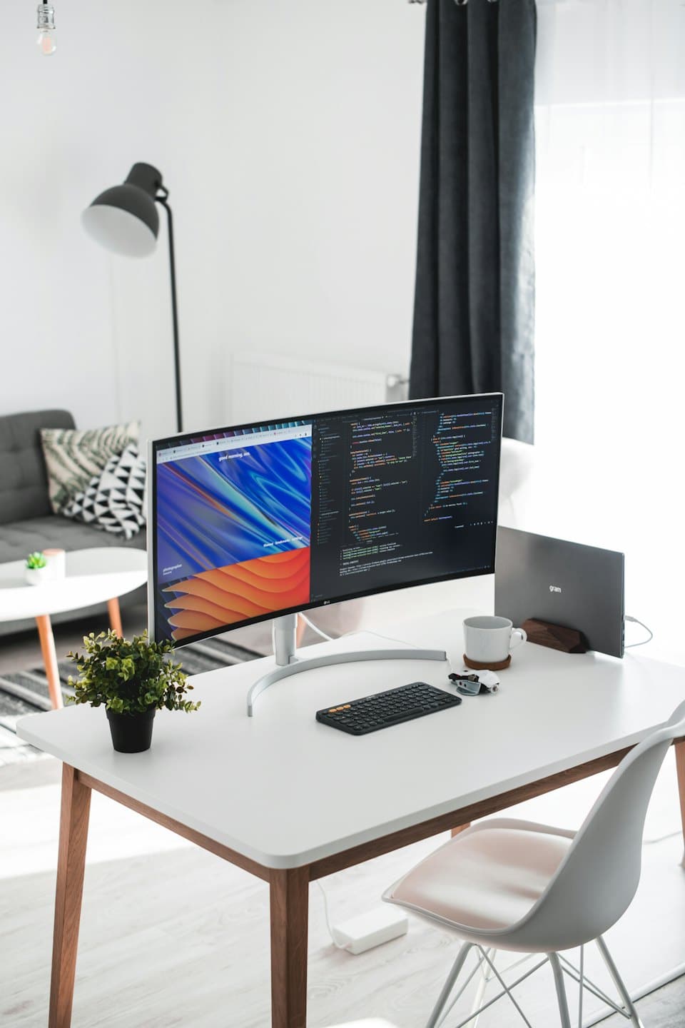 Ultrawide monitor a notebook na modernom stole s rastlinou.